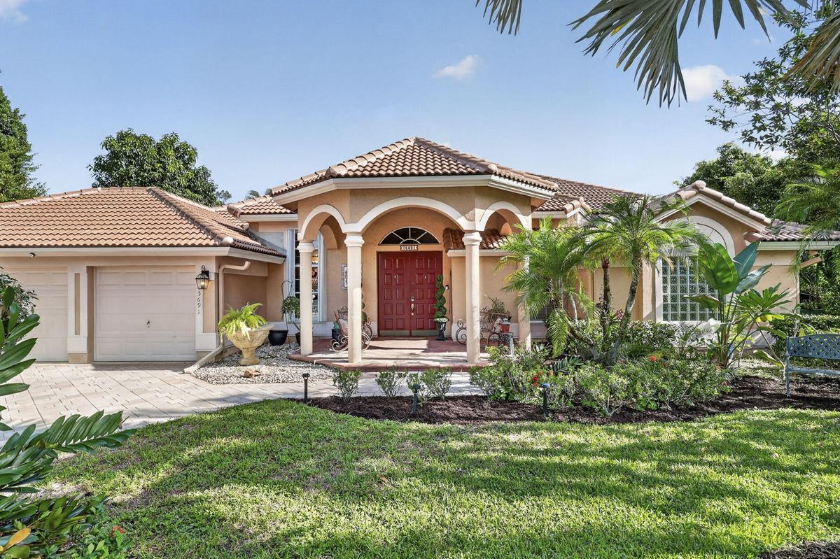 Mediterranean-style residence featuring a tile roof, arched entryway with columns, red double entry doors, a two-car garage, and mature landscaping