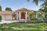 Mediterranean-style residence featuring a tile roof, arched entryway with columns, red double entry doors, a two-car garage, and mature landscaping