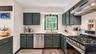 Kitchen with dark green cabinetry, white subway tile backsplash, light-colored countertops, and stainless steel appliances