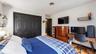 Hardwood-style flooring, dark paneled bi-fold closet doors, wall-mounted light fixture, wall-mounted shelving unit, ceiling-mounted vent