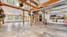 Spacious garage featuring exposed wood beams, multiple windows, a concrete floor, and built-in shelving