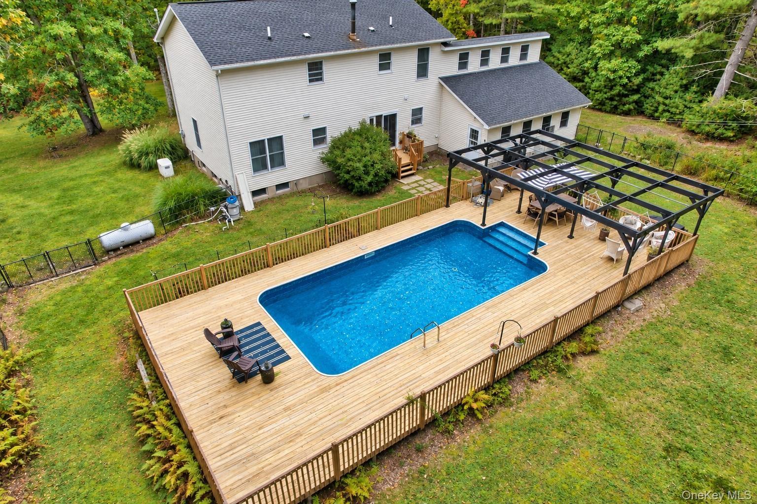 Expansive wooden deck surrounding a built-in swimming pool with steps, featuring a black metal pergola and wooden fencing