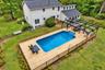 Expansive wooden deck surrounding a built-in swimming pool with steps, featuring a black metal pergola and wooden fencing