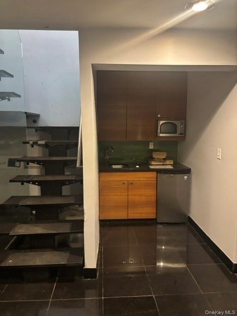 Floating staircase with glass railing, kitchen area with dark wood-finish cabinetry, stainless steel microwave, stainless steel compact refrigerator, 