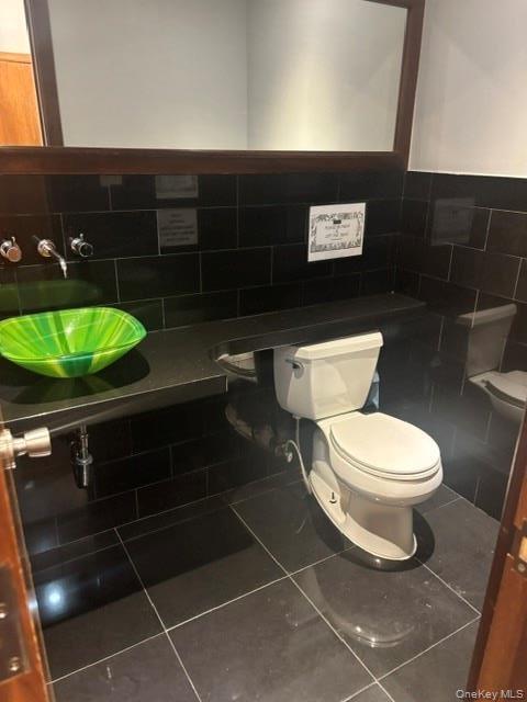 Wall-mounted faucets, vessel sink, full vanity mirror with wood frame, dark tile flooring, and dark subway tile wainscoting