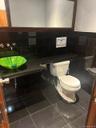 Wall-mounted faucets, vessel sink, full vanity mirror with wood frame, dark tile flooring, and dark subway tile wainscoting