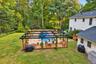 Expansive backyard featuring an in-ground swimming pool, surrounding wood-finish deck, and black metal pergola