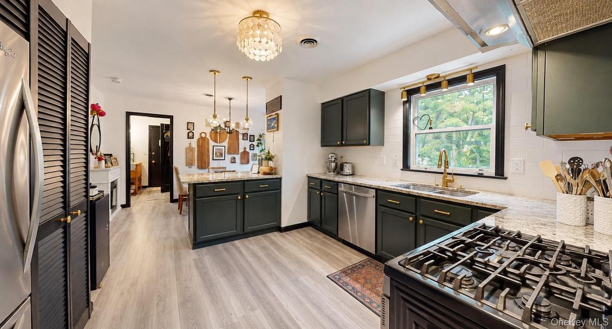 Stainless steel refrigerator, dark cabinetry with brass hardware, light wood-finish flooring, white subway tile backsplash, and light-toned countertop