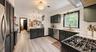 Stainless steel refrigerator, dark cabinetry with brass hardware, light wood-finish flooring, white subway tile backsplash, and light-toned countertop