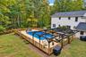 Expansive backyard featuring an in-ground pool, a surrounding wood deck, a wood privacy fence, and a dark-toned pergola