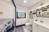 Light-toned wood-finish flooring, white vanity with integrated sink, rectangular framed mirror, and a brass-finish vanity light fixture