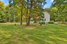 Expansive green lawn, mature trees, wood fence, natural landscaping, and a tan-sided residence