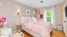 Hardwood flooring, geometric pattern accent wall, brass wall sconces, ceiling-mounted vent, and a single window with a gold-tone curtain rod