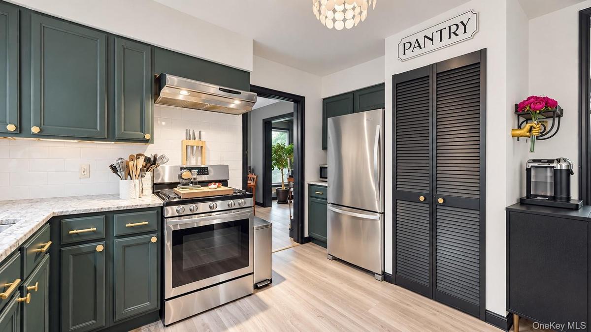 Stainless steel appliances, dark cabinetry with brass hardware, light wood-finish flooring, white subway tile backsplash, and a built-in pantry with l