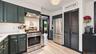 Stainless steel appliances, dark cabinetry with brass hardware, light wood-finish flooring, white subway tile backsplash, and a built-in pantry with l