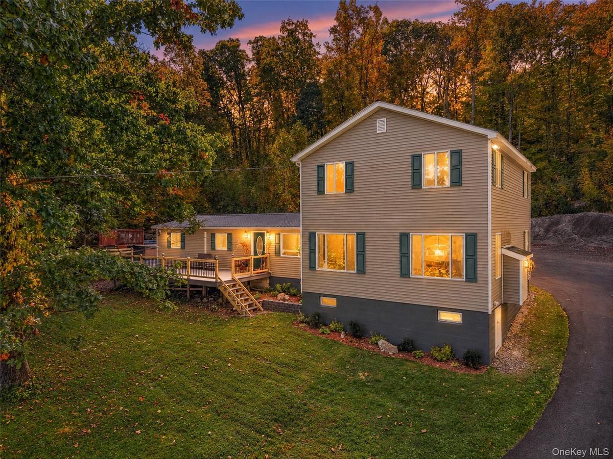 Siding exterior with multiple windows, an expansive deck, mature trees, and a paved driveway