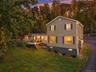 Siding exterior with multiple windows, an expansive deck, mature trees, and a paved driveway