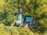 Lush natural surroundings with mature trees, multiple outbuildings, an above-ground pool with surrounding decking, and a paved driveway