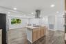 Kitchen island with a built-in gas cooktop, stainless steel range hood, wood-finish flooring, recessed lighting, and white walls
