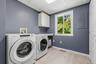 Spacious laundry room featuring wood-finish flooring, white cabinetry, a large window, and a built-in folding counter