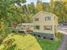 Exterior featuring light-colored siding, green window shutters, a deck, and a sloping paved driveway