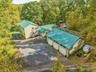 Multiple structures with green metal roofing, extensive paved driveway, and a multi-car garage with three bays
