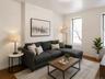 Living area with abundant natural light, featuring wood-finish flooring and crisp white walls (virtually staged)