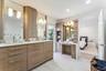 Spa-inspired primary bathroom suite featuring dual wood-finish vanities with white quartz countertops, integrated vessel sinks, and chrome fixtures