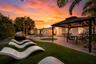 Luxurious outdoor entertaining space featuring a manicured lawn, curved lounge seating, and a pergola-covered dining area with integrated lighting