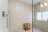 Walk-in shower featuring textured wall tiling, a rainfall showerhead, a hand-held shower fixture, and pebble-finish flooring