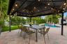 Elegant covered patio featuring a black metal gable roof with integrated pendant lighting and ceiling fans, anchoring a spacious brick-paved entertain