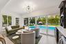 Sophisticated poolside living space featuring expansive sliding glass doors, light wood-finish flooring, and seamless indoor-outdoor connectivity