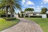 Elegant residence featuring a curved brick paver driveway, mature palm trees, and lush manicured landscaping
