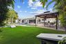 Expansive backyard oasis featuring manicured lawn, mature landscaping with specimen trees, and a modern pergola-covered entertaining area with dining 