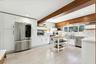 Spacious kitchen featuring vaulted ceilings with exposed wood beams, stainless steel appliances, white cabinetry, and a tile backsplash