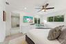 Bright primary bedroom featuring a wood-finish plank floor, ceiling fan with integrated lighting, and abundant natural light from dual windows