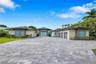 Paver stone driveway featuring an gated entrance with vertical fencing, mature palm trees, and wall-mounted exterior lighting
