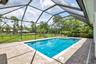 Screened-in outdoor living space featuring a geometric swimming pool with integrated spa, paver patio, and a backdrop of mature trees
