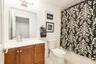Bathroom featuring a wood-finish vanity with a white countertop and integrated sink, brushed nickel faucet, wall-mounted mirror, and overhead vanity l