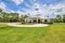 Spacious property featuring a white exterior residence with a covered entryway, a circular driveway, mature landscaping, and a surrounding privacy fen