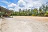 Expansive outdoor arena featuring a sand surface, perimeter fencing, and mature tropical landscaping