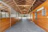 Spacious barn interior featuring exposed wood beams and ceiling, multiple stalls with custom stall doors, center isle, fans, fly system, 3 stalls have