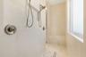 Spacious shower featuring light-toned tile walls, dual shower heads with brushed nickel fixtures, a built-in bench with veined stone, pebble-finish fl