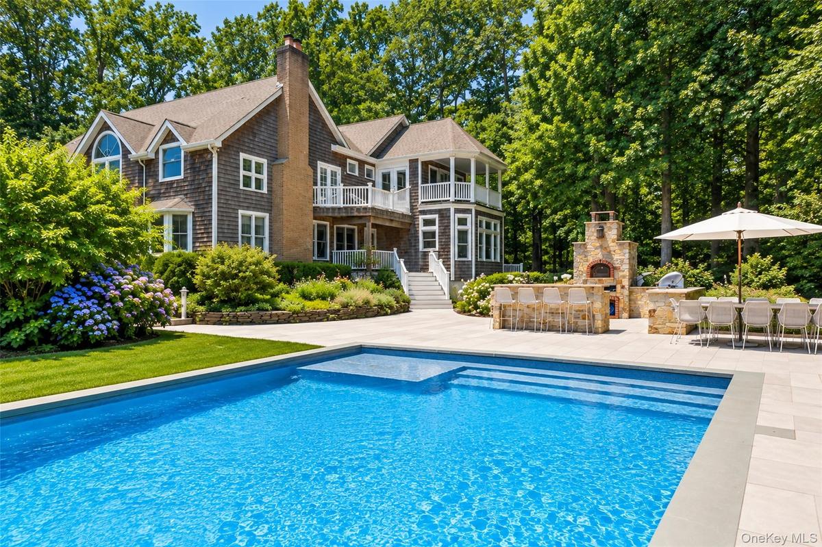 Shingle-sided residence with multiple balconies, a spacious patio, a built-in outdoor kitchen with a stone-clad pizza oven, a rectangular swimming poo