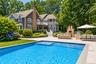 Shingle-sided residence with multiple balconies, a spacious patio, a built-in outdoor kitchen with a stone-clad pizza oven, a rectangular swimming poo