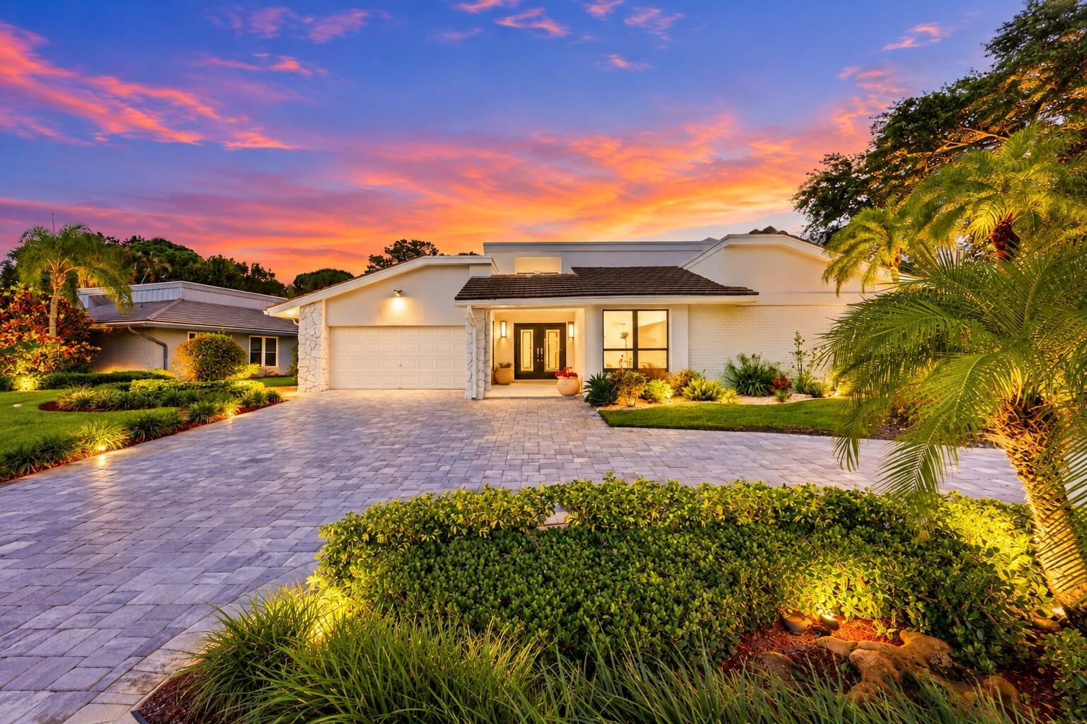 A striking first impression begins with a sweeping paver driveway, lush tropical landscaping, and timeless architectural details that set this home ap