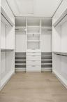 The custom walk-in closet is thoughtfully designed with extensive built-in storage, adjustable shelving, multiple hanging areas, and dedicated drawer 
