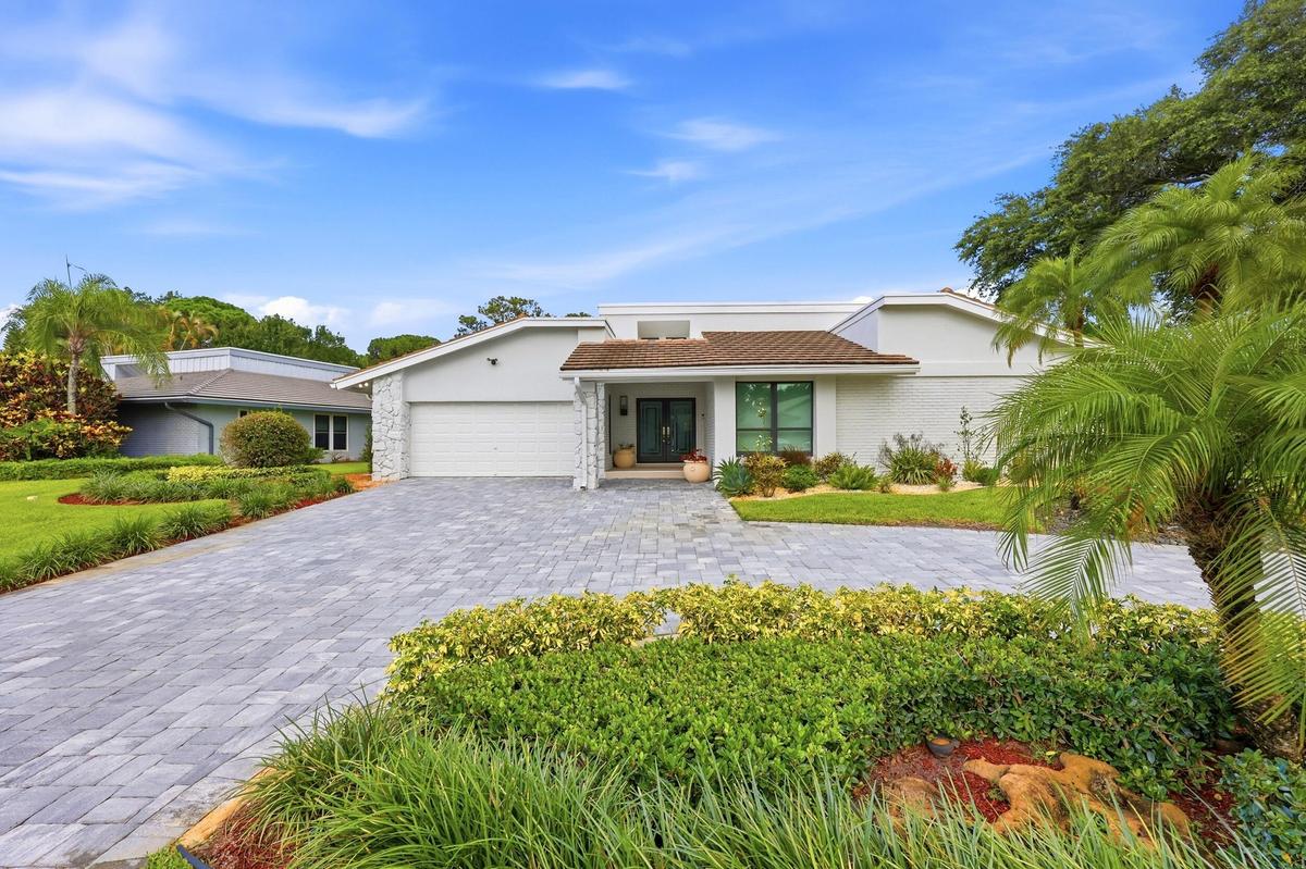 A striking first impression begins with a sweeping paver driveway, lush tropical landscaping, and timeless architectural details that set this home ap