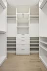 The custom walk-in closet is thoughtfully designed with extensive built-in storage, adjustable shelving, multiple hanging areas, and dedicated drawer 