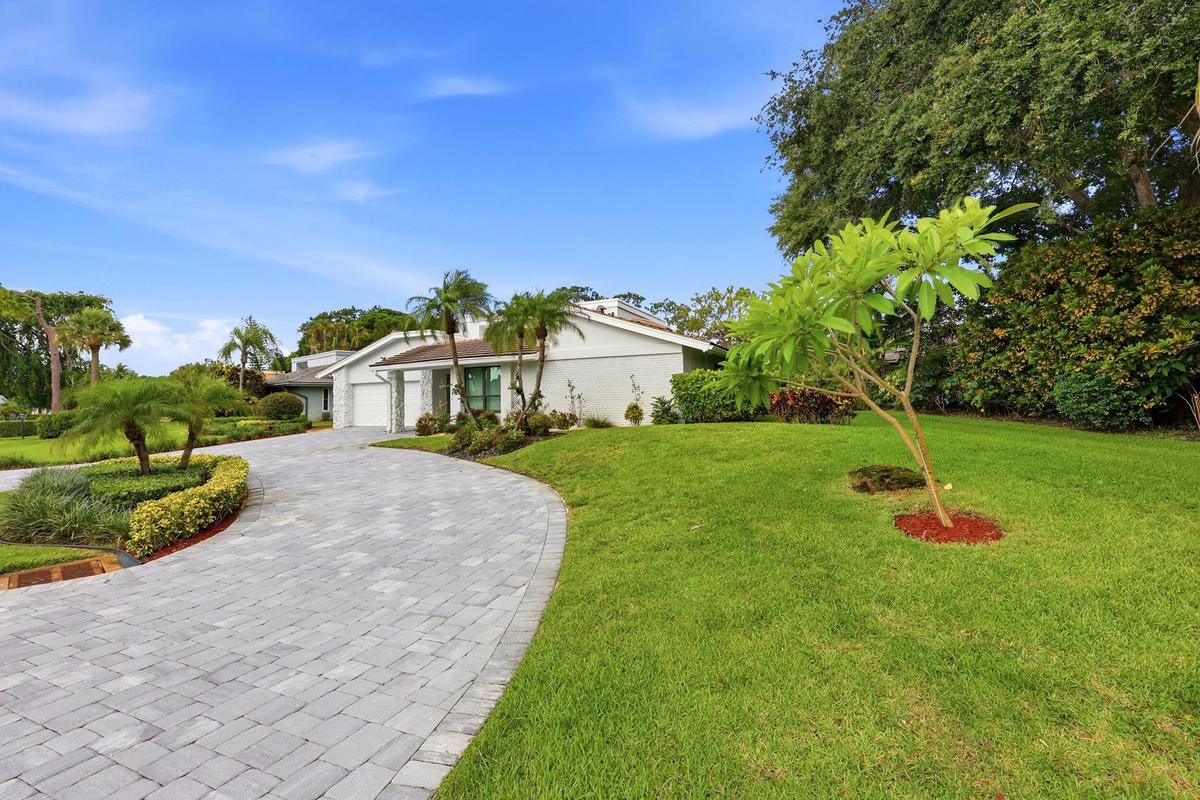 A striking first impression begins with a sweeping paver driveway, lush tropical landscaping, and timeless architectural details that set this home ap